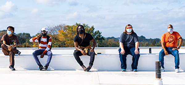 five people sitting on a wall wearing masks