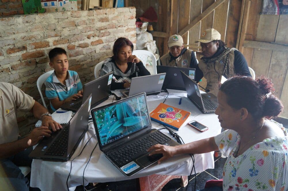 A diverse group of individuals sitting around a table, engrossed in their work on laptops.