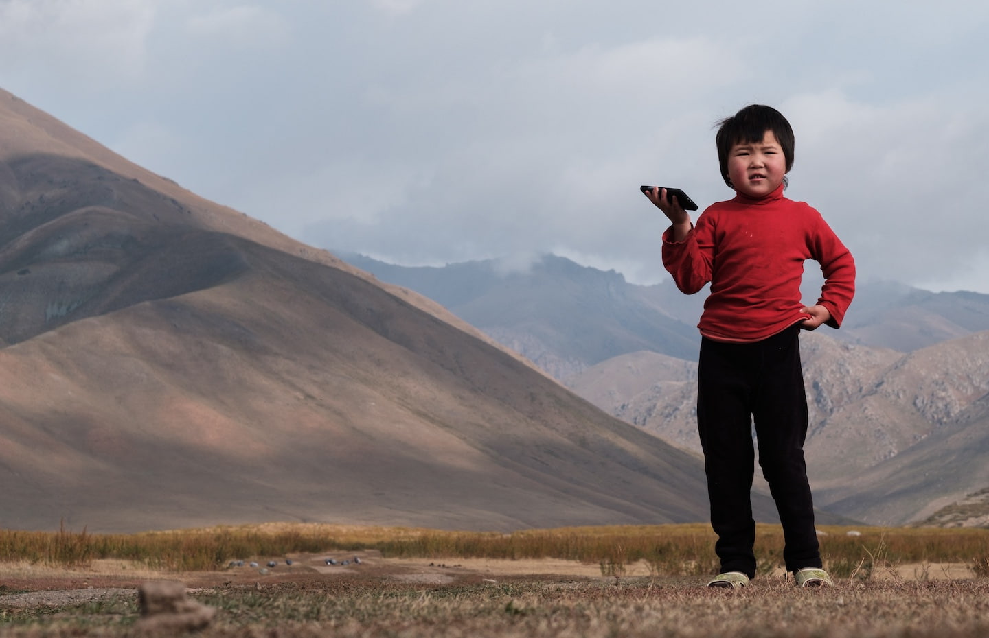 A child wearing a red shirt stands confidently in a lush green field, surrounded by nature.